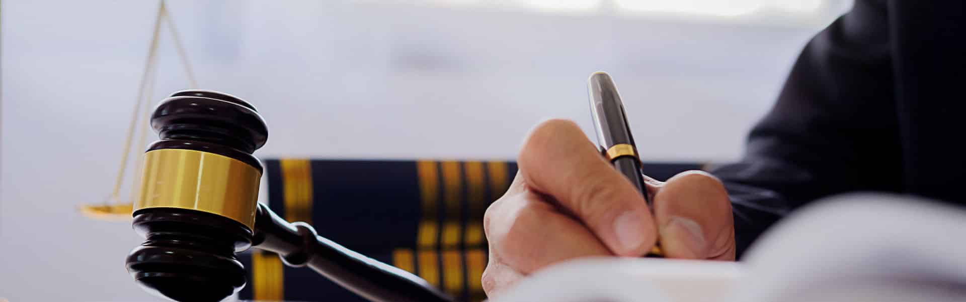 A lawyer signs papers beside a judge’s gavel