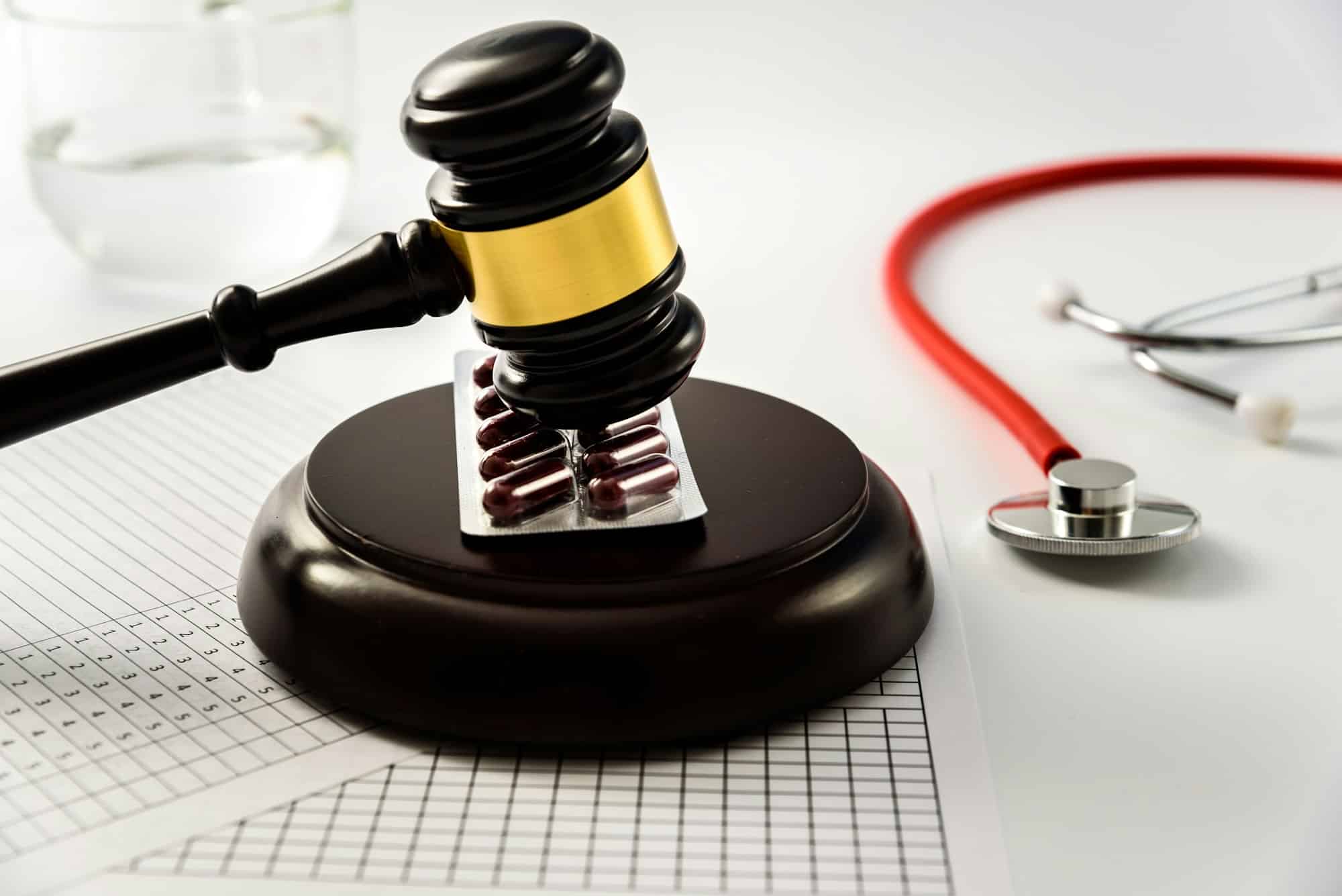 A judge’s gavel on a pack of pills beside a stethoscope