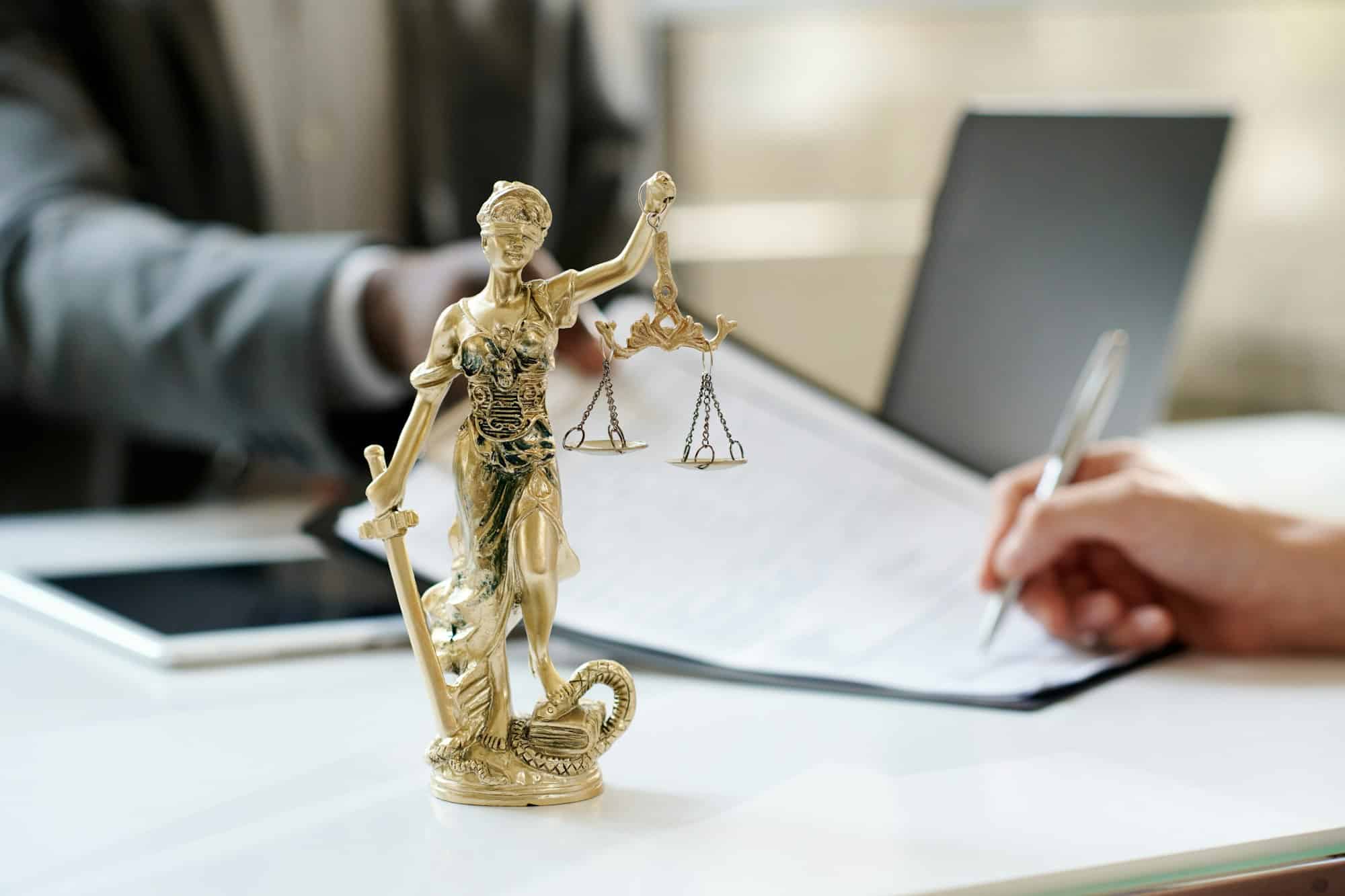 A Lady Justice statuette on a desk while a client signs a document