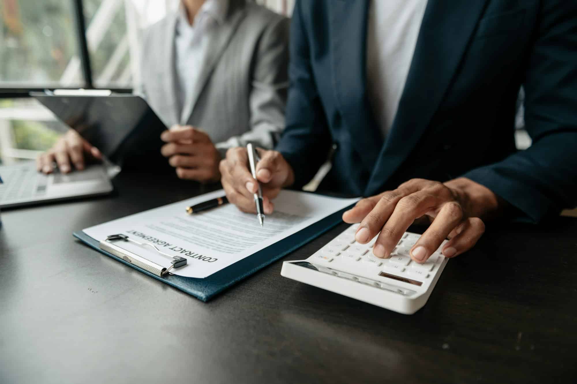 An adviser and a client review a contract agreement with a calculator